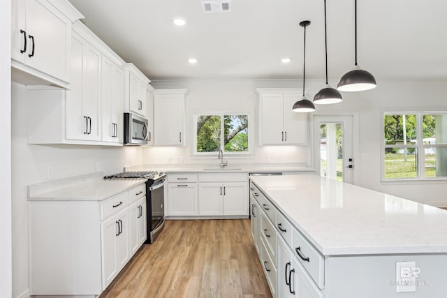 5099 Leeward Dr, Pensacola, FL 32507 - kitchen featuring appliances with stainless steel finishes, a sink, light wood-type flooring, a kitchen island, and white cabinets