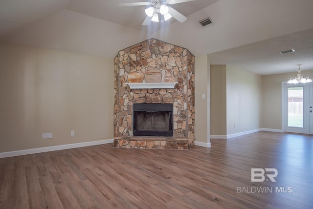 unfurnished living room with hardwood / wood-style flooring, vaulted ceiling, a stone fireplace, and ceiling fan with notable chandelier