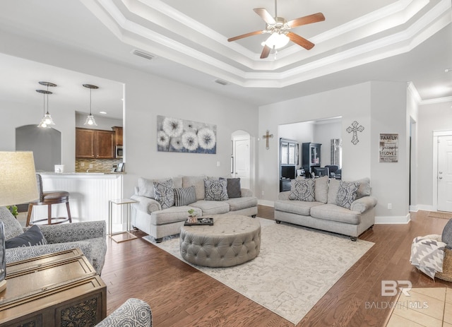 living room with a raised ceiling, crown molding, dark wood-type flooring, and ceiling fan