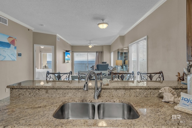 kitchen featuring crown molding, ceiling fan, light stone countertops, a textured ceiling, and a sink