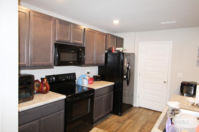 kitchen with light hardwood / wood-style floors, dark brown cabinets, and black appliances