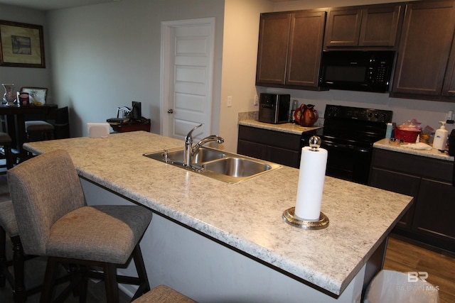 kitchen featuring sink, dark brown cabinets, dark hardwood / wood-style floors, black appliances, and an island with sink