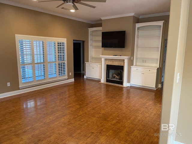 unfurnished living room with a tiled fireplace, ceiling fan, crown molding, and dark wood-type flooring