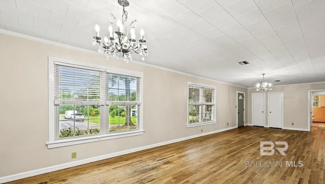 unfurnished dining area with hardwood / wood-style floors, crown molding, and an inviting chandelier