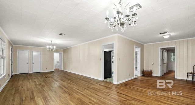 unfurnished living room featuring an inviting chandelier, ornamental molding, a wealth of natural light, and hardwood / wood-style floors