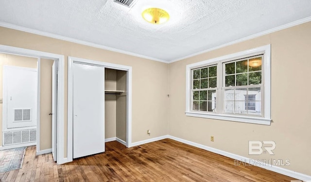 unfurnished bedroom featuring wood-type flooring, a closet, a textured ceiling, and ornamental molding