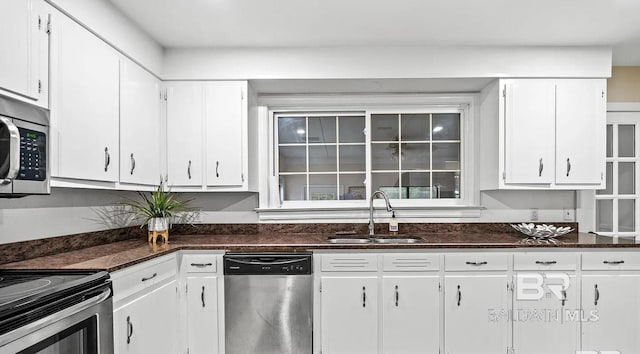 kitchen with stainless steel appliances, dark stone countertops, white cabinetry, and sink