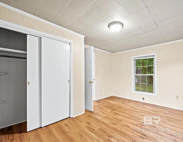 unfurnished bedroom featuring a closet, ornamental molding, and light hardwood / wood-style flooring