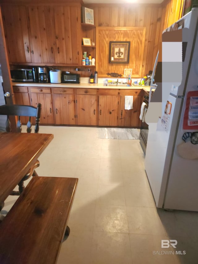 kitchen featuring brown cabinets, wood walls, a sink, and freestanding refrigerator