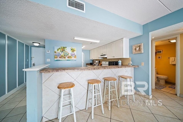 kitchen featuring white cabinets, a textured ceiling, light tile patterned floors, and kitchen peninsula