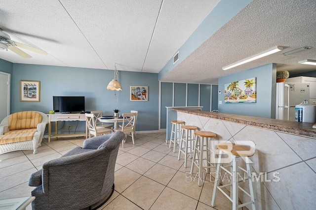 tiled dining area with a textured ceiling, ceiling fan, and bar