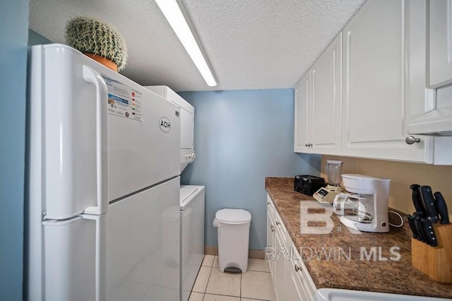 kitchen featuring light tile patterned floors, a textured ceiling, dark stone countertops, white cabinetry, and white fridge