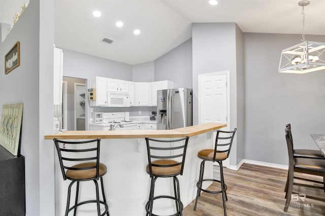 kitchen featuring white appliances, butcher block counters, a chandelier, a kitchen bar, and white cabinetry
