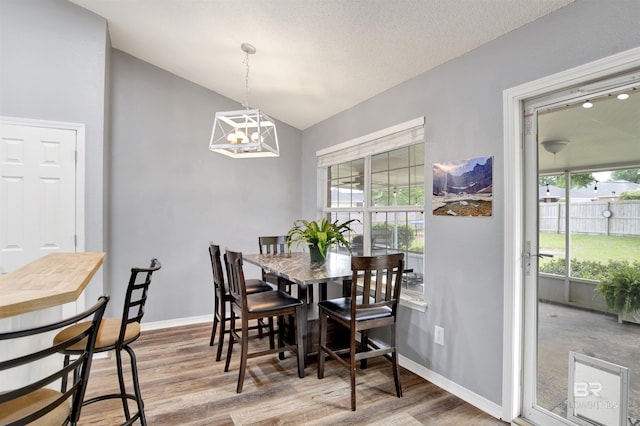 dining area featuring lofted ceiling, wood finished floors, a chandelier, and baseboards
