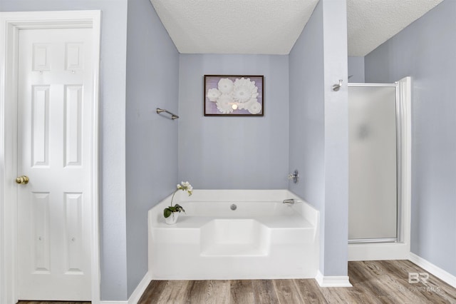 bathroom featuring a garden tub, a shower stall, wood finished floors, a textured ceiling, and baseboards