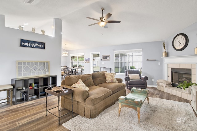 living room with ceiling fan, wood finished floors, vaulted ceiling, a tile fireplace, and baseboards