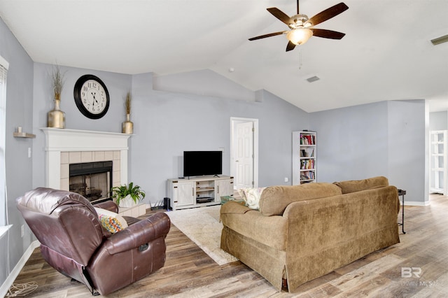 living area featuring ceiling fan, wood finished floors, a tiled fireplace, lofted ceiling, and baseboards