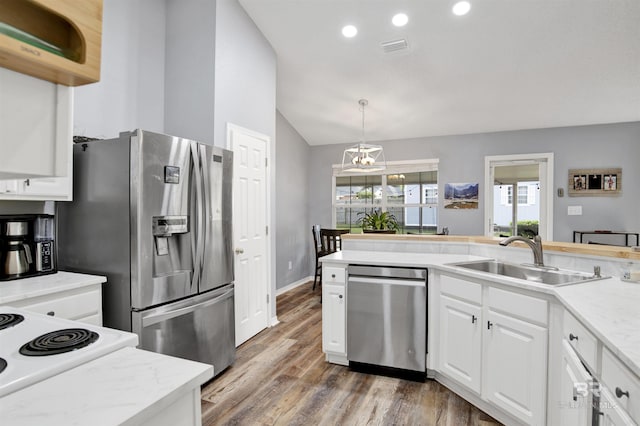 kitchen featuring stainless steel appliances, a sink, a chandelier, vaulted ceiling, and white cabinets