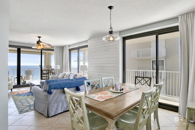 dining area featuring a water view, light tile patterned floors, ceiling fan, and a textured ceiling