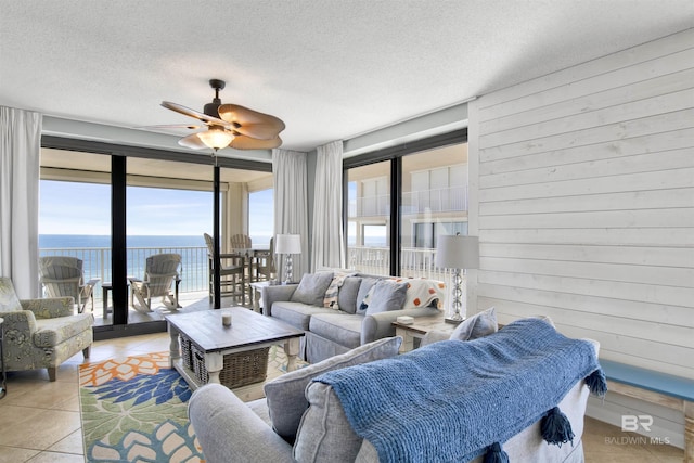 living area with a textured ceiling, a water view, tile patterned flooring, and wooden walls