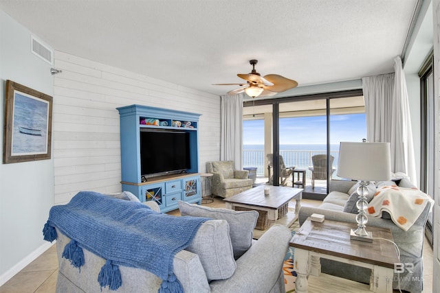 tiled living area featuring a ceiling fan, visible vents, wood walls, and a textured ceiling