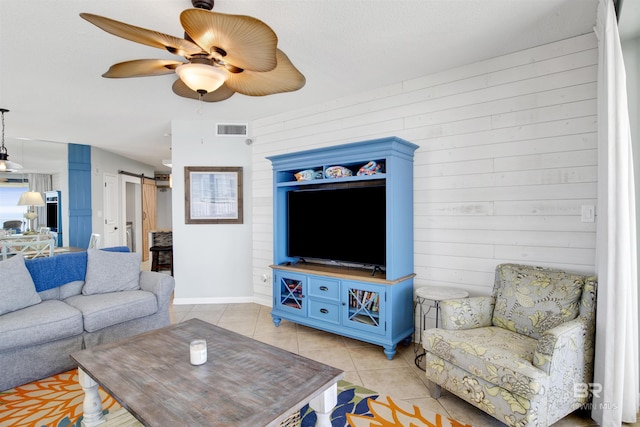 living area featuring light tile patterned floors, visible vents, a barn door, ceiling fan, and wooden walls