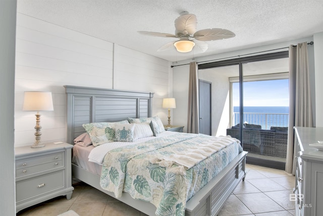 bedroom featuring a textured ceiling, light tile patterned flooring, a water view, a ceiling fan, and access to exterior