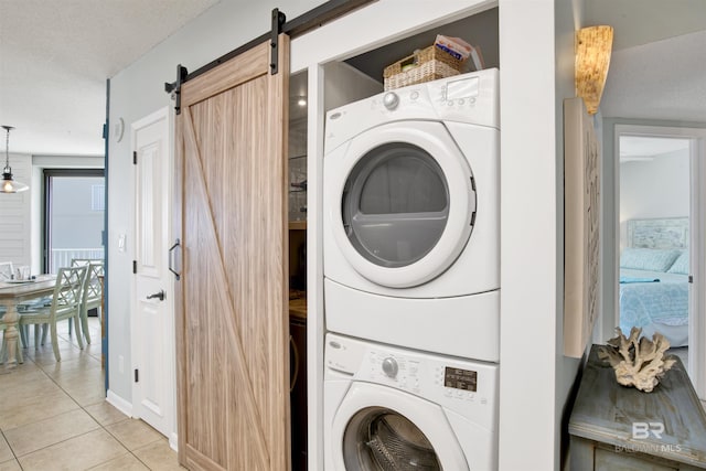 clothes washing area featuring stacked washer and clothes dryer, light tile patterned flooring, and a barn door