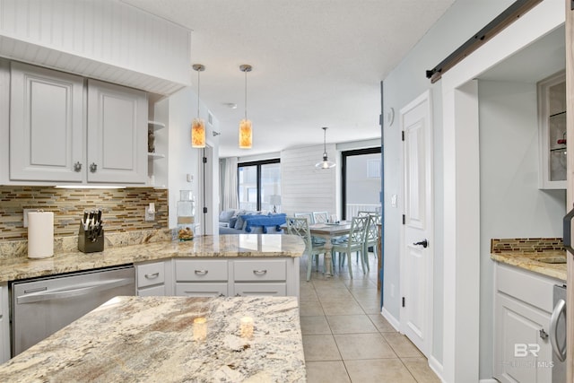 kitchen featuring light tile patterned floors, a barn door, tasteful backsplash, and stainless steel dishwasher