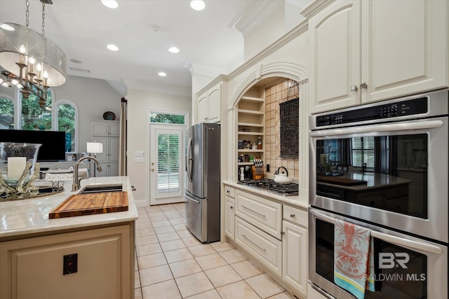 kitchen featuring light tile patterned floors, appliances with stainless steel finishes, ornamental molding, decorative light fixtures, and a chandelier