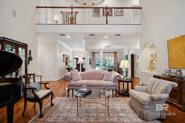 living room with ornamental molding, a high ceiling, light hardwood / wood-style flooring, and ornate columns