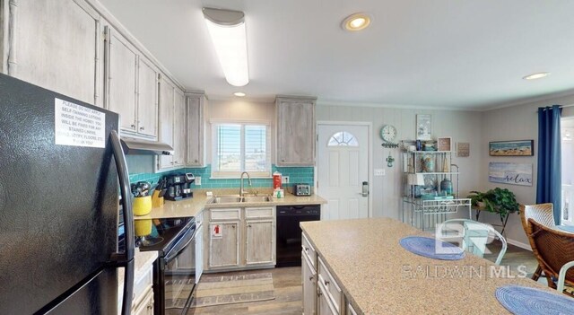 kitchen with light wood-type flooring, sink, tasteful backsplash, and black appliances