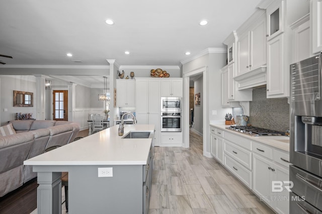 kitchen with a sink, open floor plan, light countertops, appliances with stainless steel finishes, and ornate columns