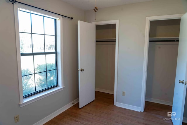 unfurnished bedroom with baseboards, wood finished floors, and multiple closets