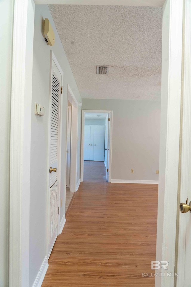 hall with light wood finished floors, baseboards, visible vents, and a textured ceiling