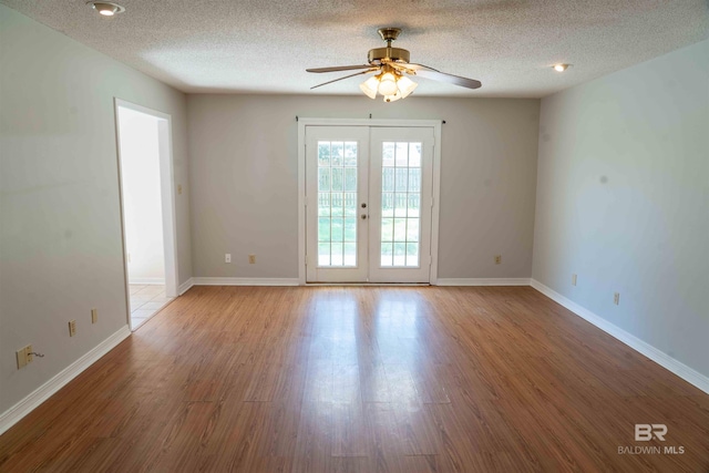 empty room with a textured ceiling, baseboards, wood finished floors, and french doors