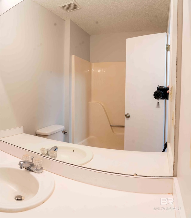 bathroom featuring a textured ceiling, visible vents, a shower, and a sink