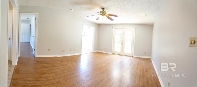 spare room featuring a textured ceiling, french doors, baseboards, and light wood-style floors