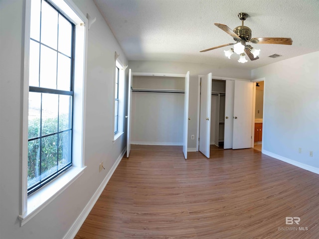 unfurnished bedroom featuring a textured ceiling, wood finished floors, visible vents, and multiple closets