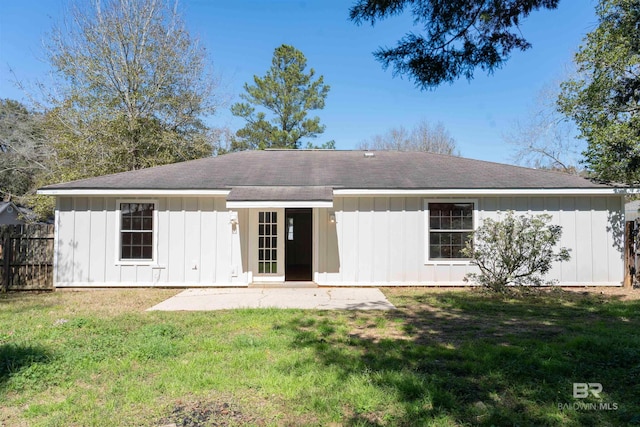 back of property with board and batten siding, fence, and a lawn