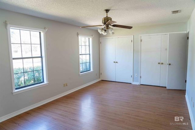 unfurnished bedroom featuring multiple windows, visible vents, two closets, and wood finished floors