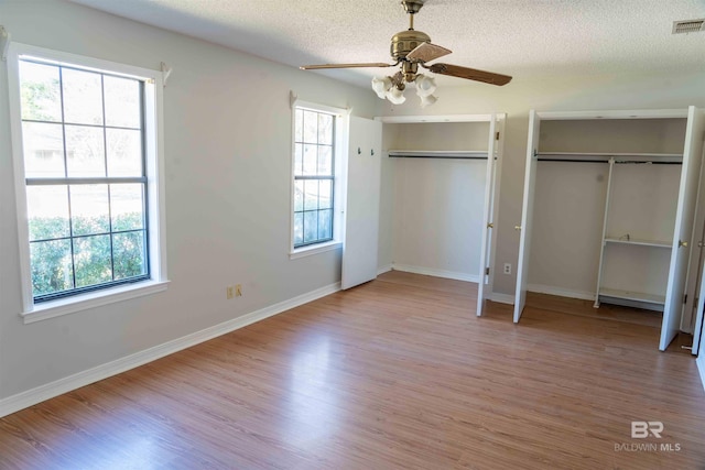 unfurnished bedroom featuring two closets, visible vents, a textured ceiling, wood finished floors, and baseboards