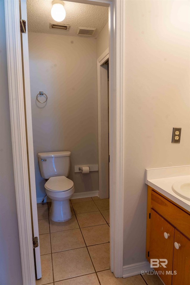 half bathroom with a textured ceiling, tile patterned flooring, toilet, vanity, and visible vents