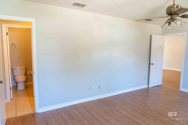 spare room featuring baseboards, visible vents, ceiling fan, wood finished floors, and a textured ceiling