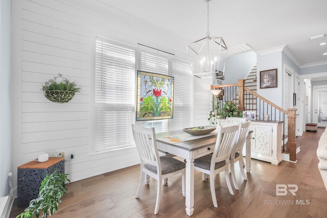 dining area featuring wood-type flooring, crown molding, wooden walls, and a chandelier