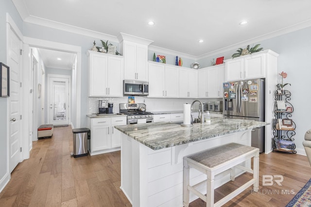 kitchen with a center island with sink, a kitchen breakfast bar, light wood-type flooring, appliances with stainless steel finishes, and white cabinetry