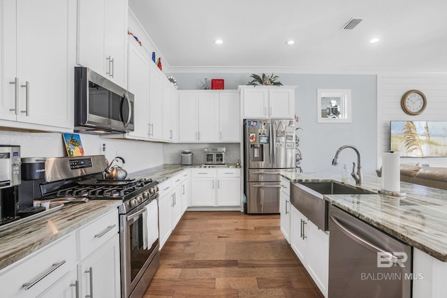 kitchen featuring light stone countertops, white cabinetry, sink, stainless steel appliances, and wood-type flooring