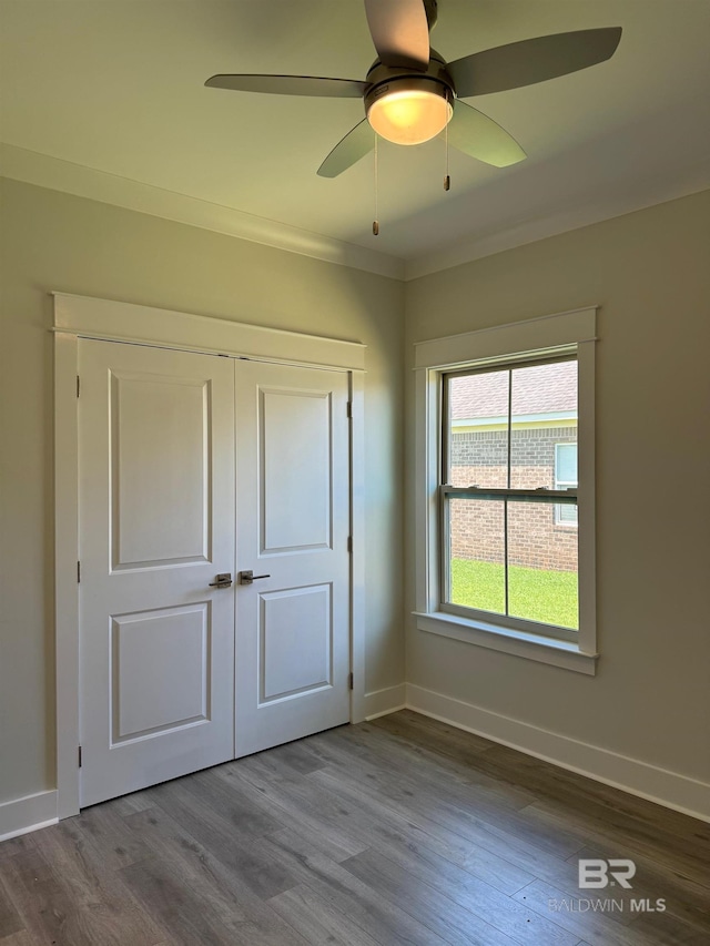 unfurnished bedroom with ceiling fan, a closet, hardwood / wood-style flooring, and crown molding