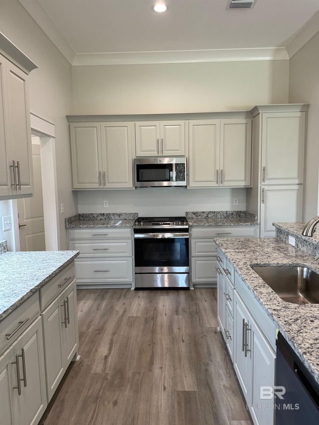 kitchen featuring crown molding, light stone countertops, stainless steel appliances, hardwood / wood-style flooring, and sink