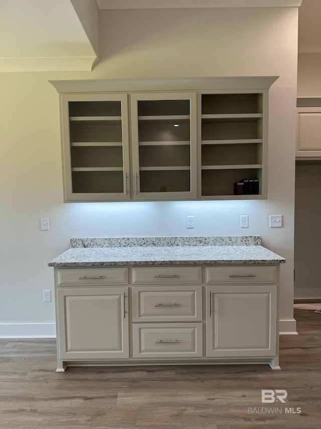 bar featuring built in features, light stone countertops, and hardwood / wood-style flooring